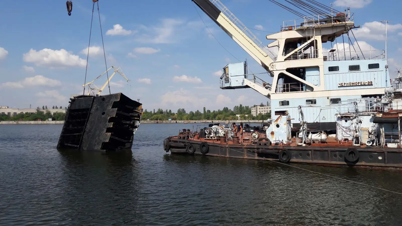 Плавкран піднімає з води секцію затонулої споруди в порту
